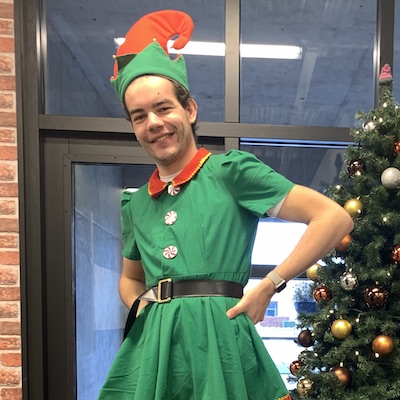 Steyn Potze, a human male, in what appears to be an elf costume near a Christmas tree. This alt text was definitely written by a human and not an AI that over-describes images.